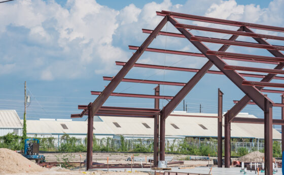 Steel structure of new industrial building under clear blue sky. New technology structural frame beam of factory in construction. Steel frame manufacturer and pile of sand and gravel in Crosby, TX, US